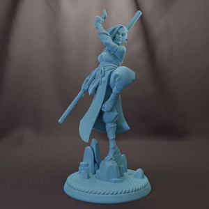A figurine of a woman in a fighting stance, holding a weapon and standing on a platform with rocks.