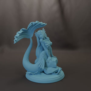 A blue mermaid figurine sitting on a rock, with a large tail extending behind her.