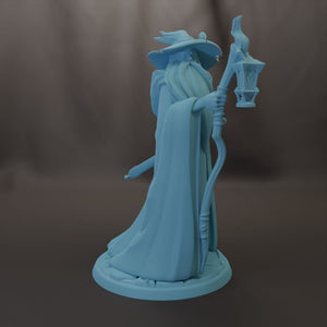 A blue 3D model of a wizard or magical figure holding a lantern and a staff, standing on a base.