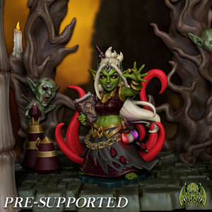 A figurine of a green-skinned, blonde-haired, and green-eyed character with a red and gold outfit, holding a book, standing in a fantasy setting with trees and other fantastical elements.
