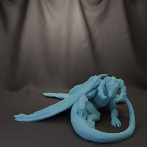 A blue dragon figurine is depicted in a crouched position, with its wings spread out, against a dark background.