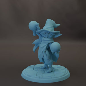 A blue figurine of a wizard or magical character holding a ball and a skull, standing on a stone base.
